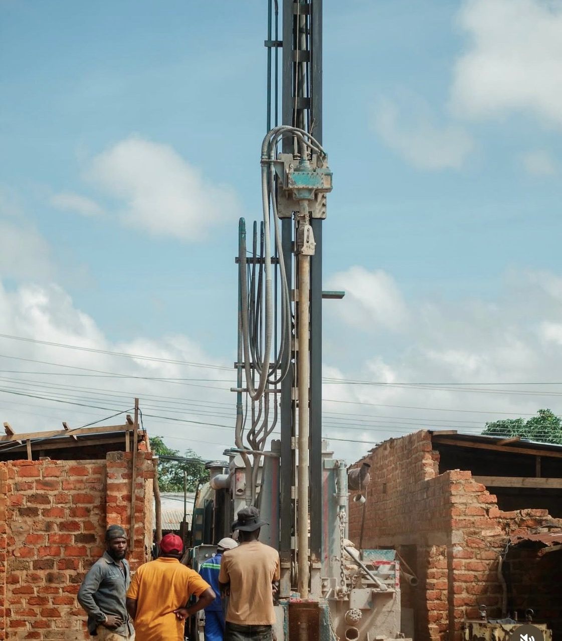 The tall borehole drilling rig rises against a blue sky between brick buildings in Lubumbashi